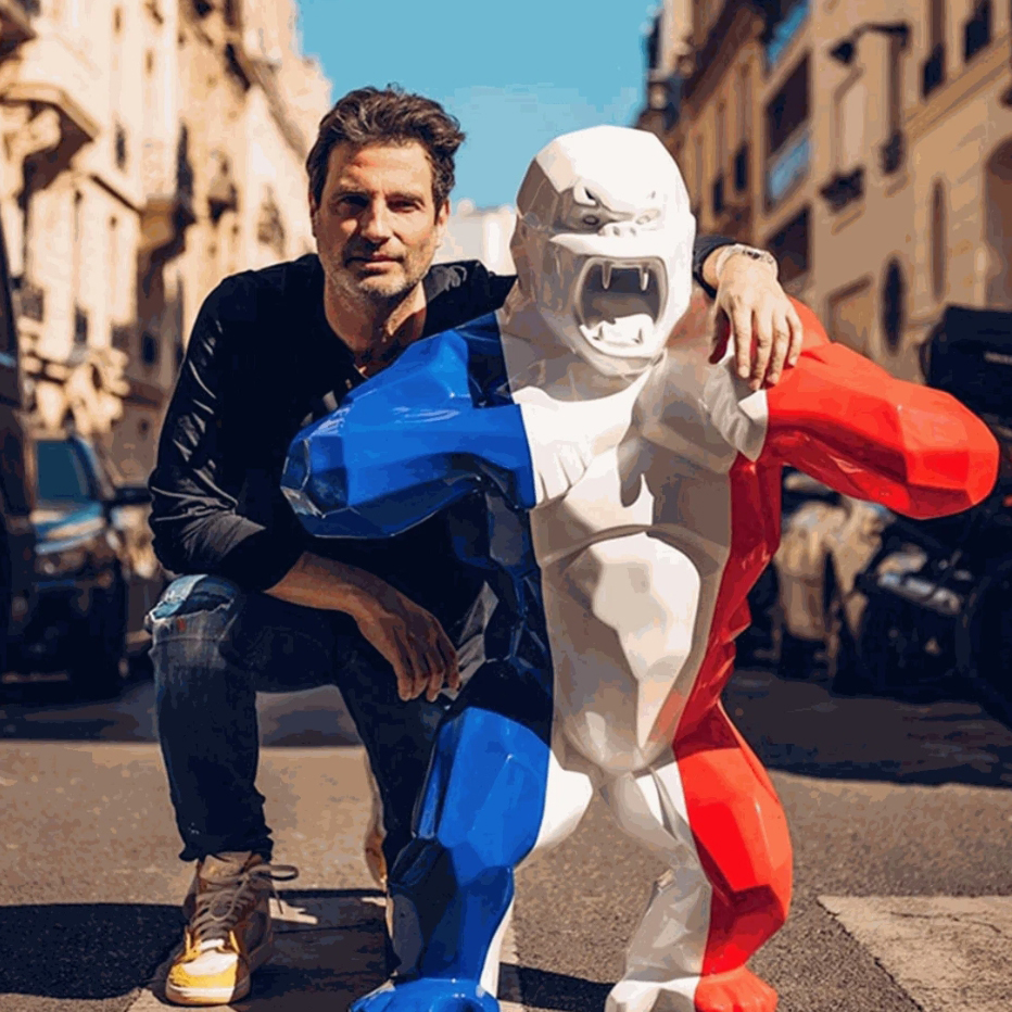 Richard Orlinski posing on the street with a red, white, and blue Wild Kong sculpture representing the French flag colors