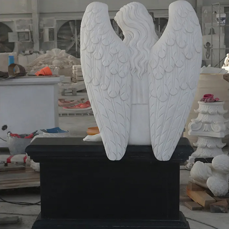 back view of Marble Angel sitting on black Headstone showing detailed feathered wings