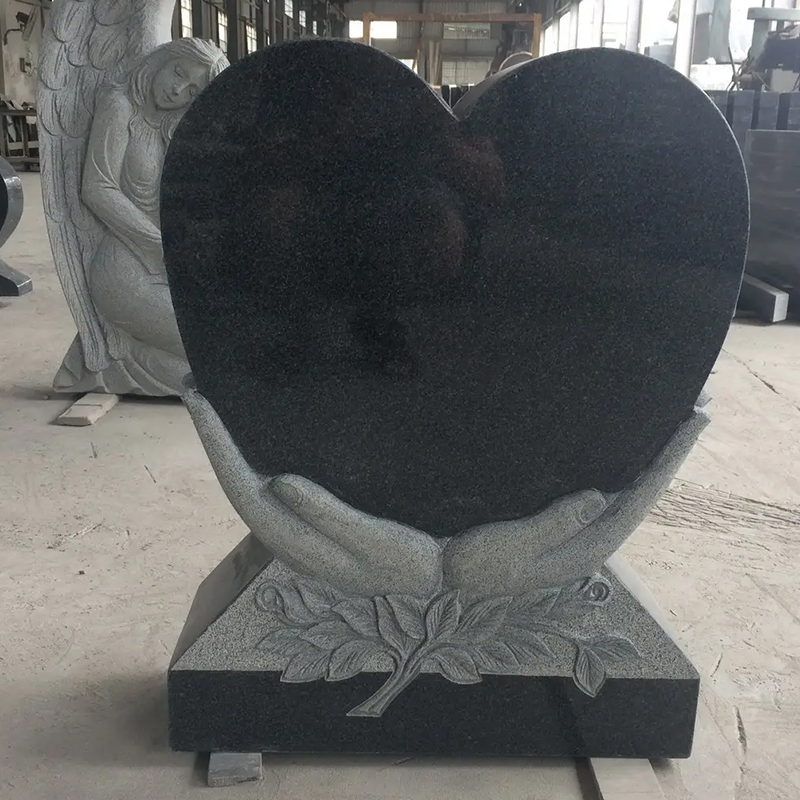 granite memorial headstone featuring a heart-shaped design held by two hands, with intricate leaf carvings at the bas