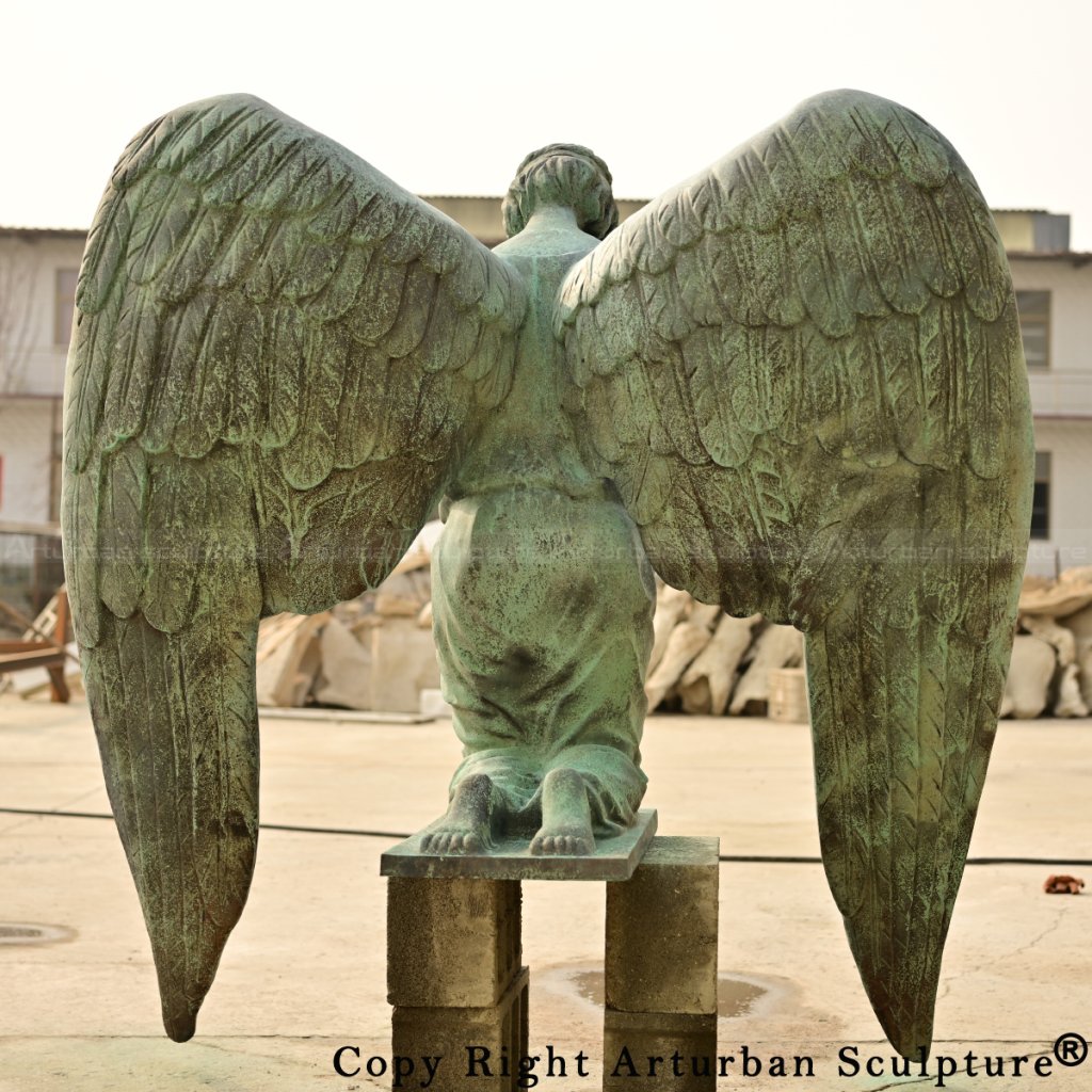 Back view of the bronze kneeling angel statue with fully extended wings and aged green patina surface