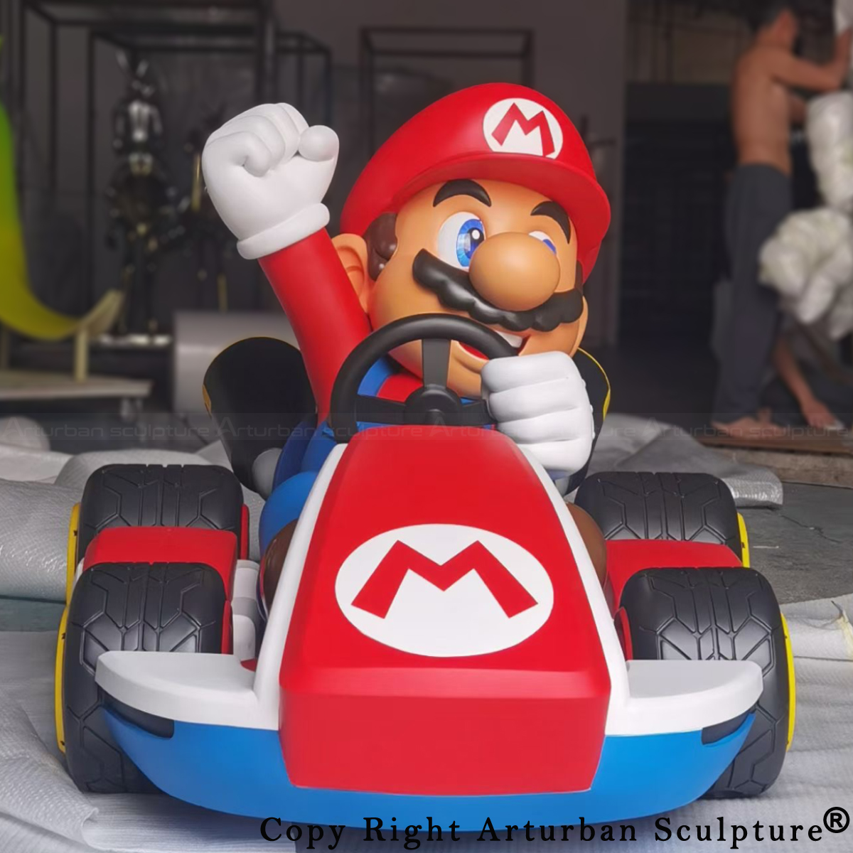 Front view of the Mario Kart statue showing Mario gripping the wheel with one hand and raising the other in a victory pose