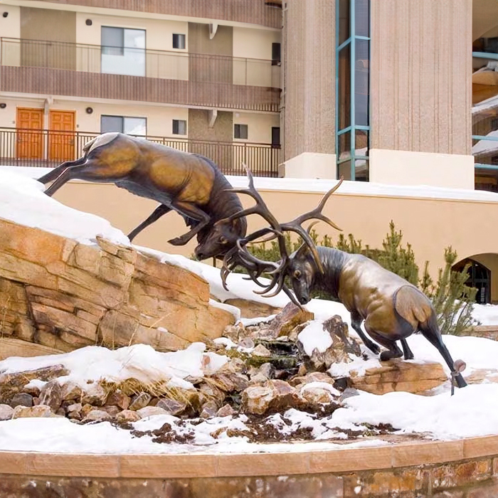 Deer Elk Statue showing two bronze male elk in a dramatic antler battle on snowy rocky terrain