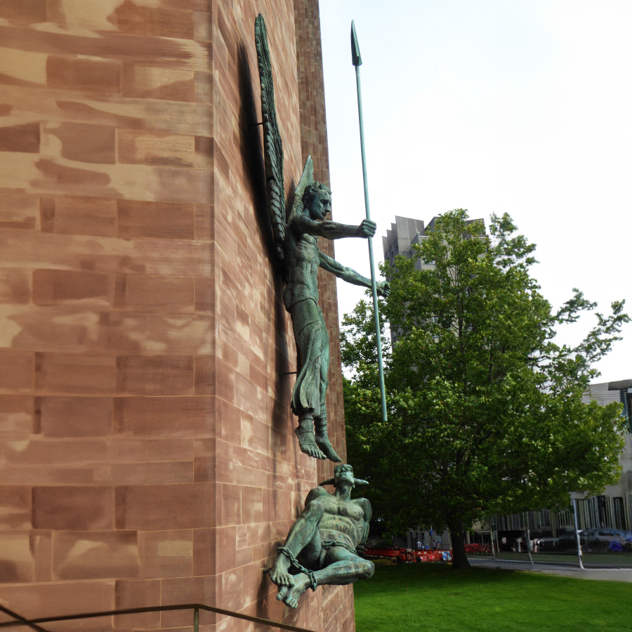 Side view of Archangel Michael and Satan sculpture mounted on the red brick wall of Coventry Cathedral