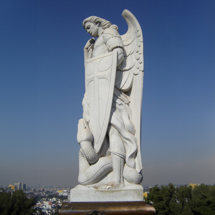 White marble statue of Saint Michael holding a shield, trampling a snake, set against the sky