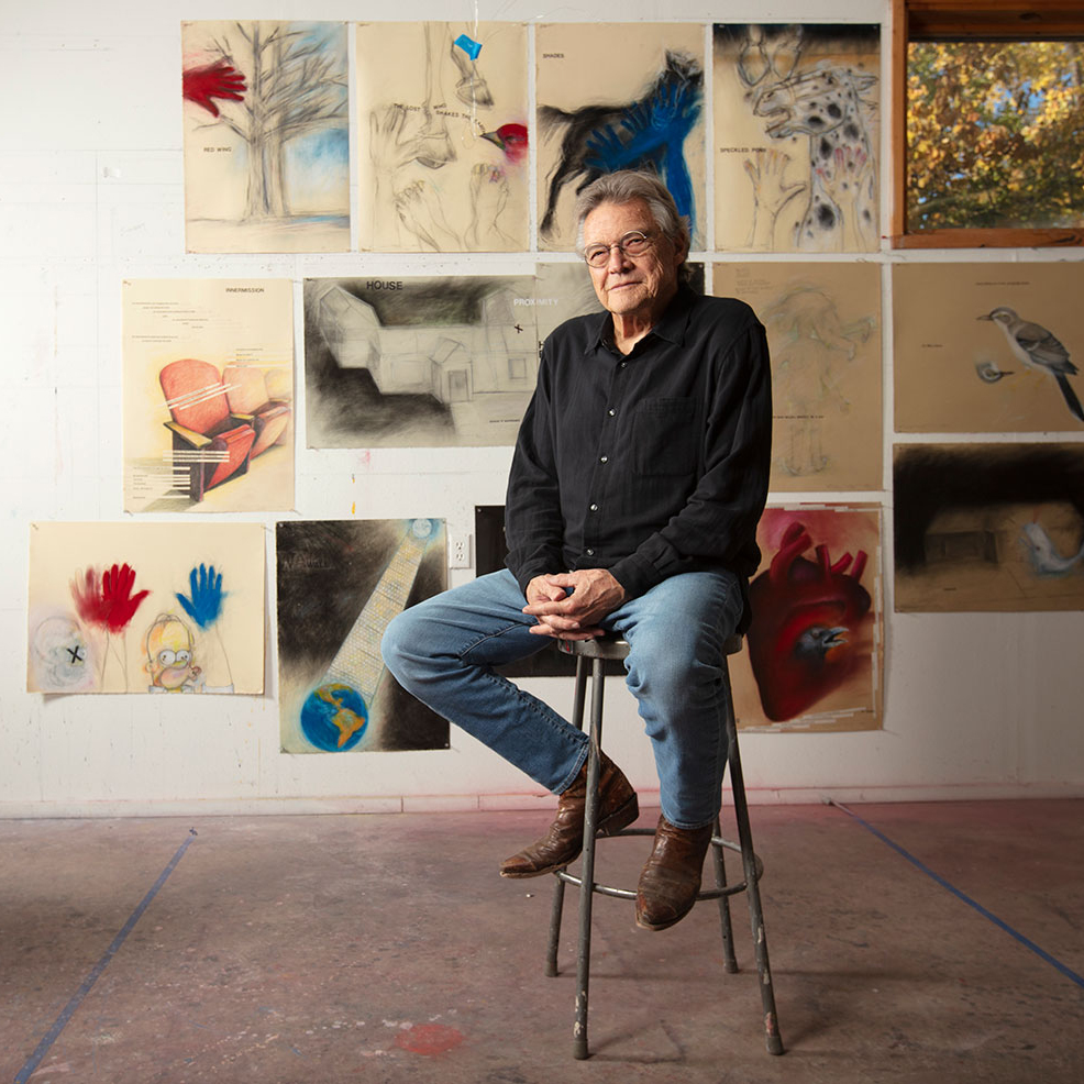 Artist Terry Allen sitting in front of his drawings