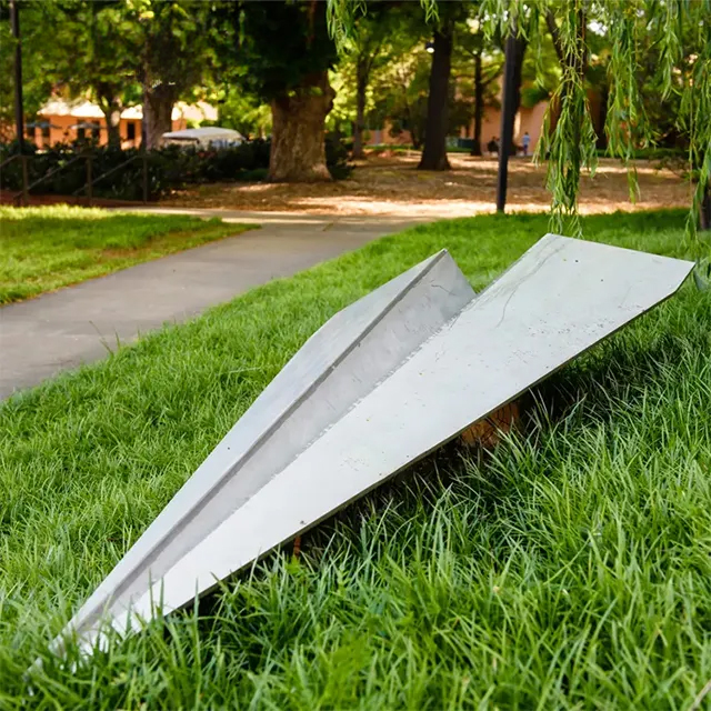 A modern Paper Plane Statue made of stainless steel displayed on grass