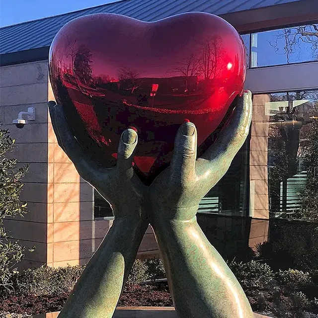 Bronze hands supporting a mirror-polished Stainless Steel Heart Sculpture
