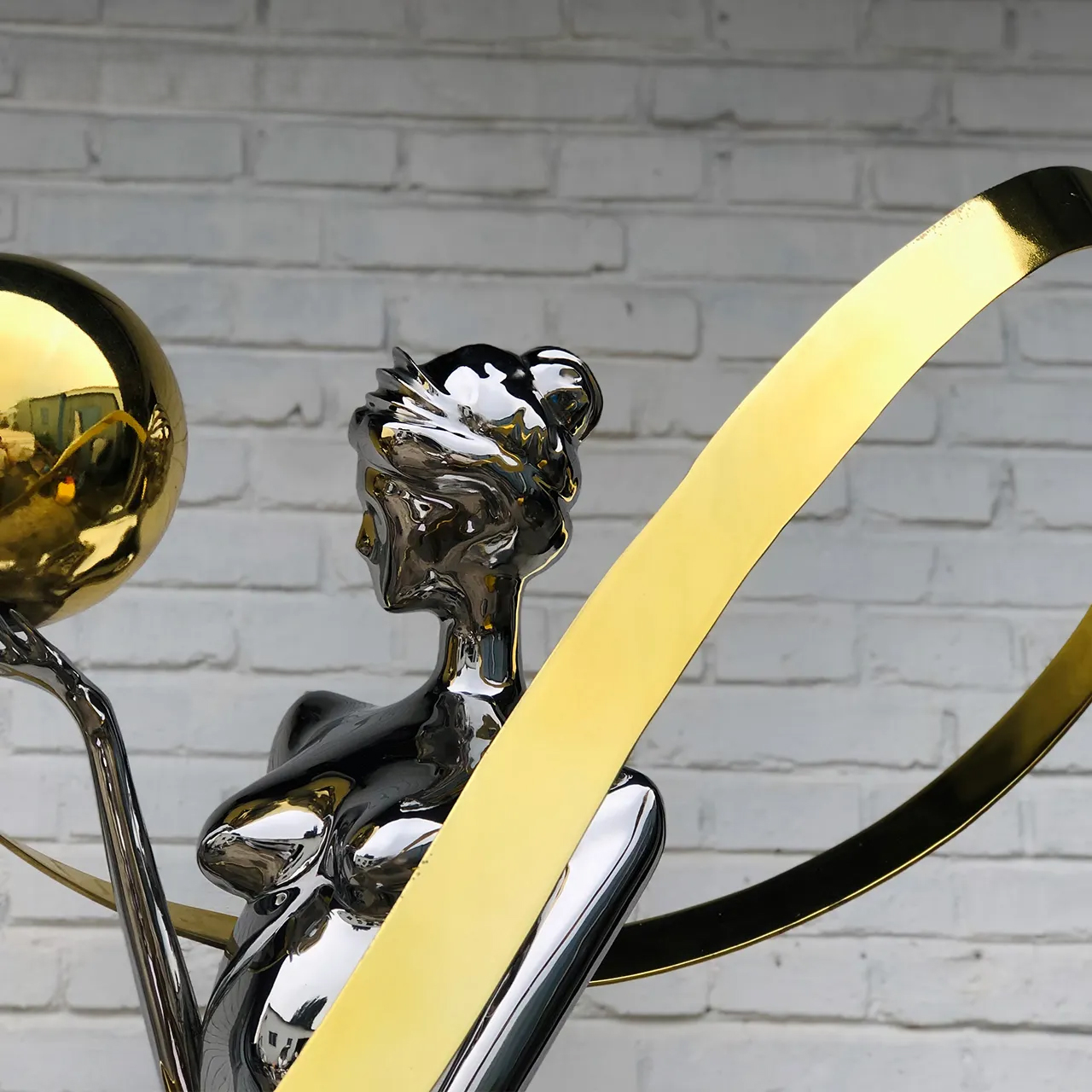 Close-up of abstract stainless steel dancing figure sculpture with golden sphere and curved ribbons
