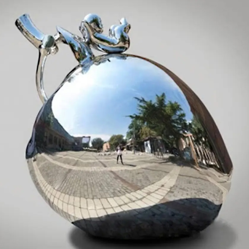 Front view of the stainless steel apple sculpture with the child figure on top