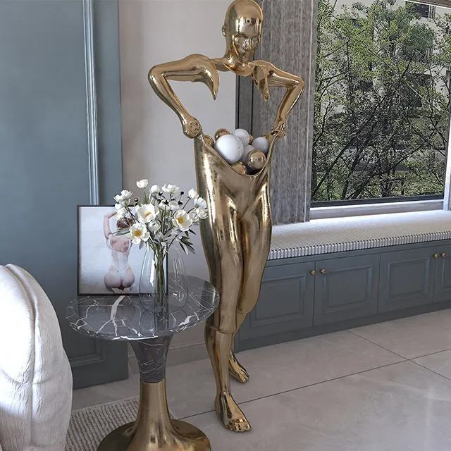 Golden Steel Man Statue presenting a modern abstract male figure pulling open his pants filled with decorative spheres