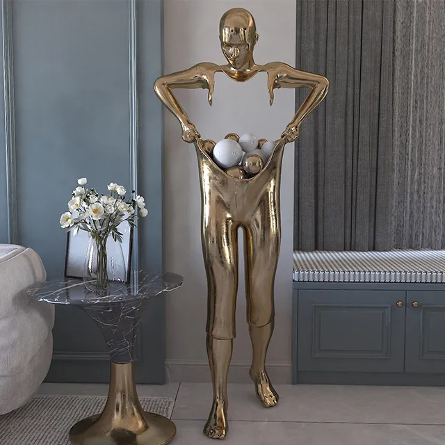 Golden stainless Steel Man Statue featuring a male figure holding open pants filled with metal spheres
