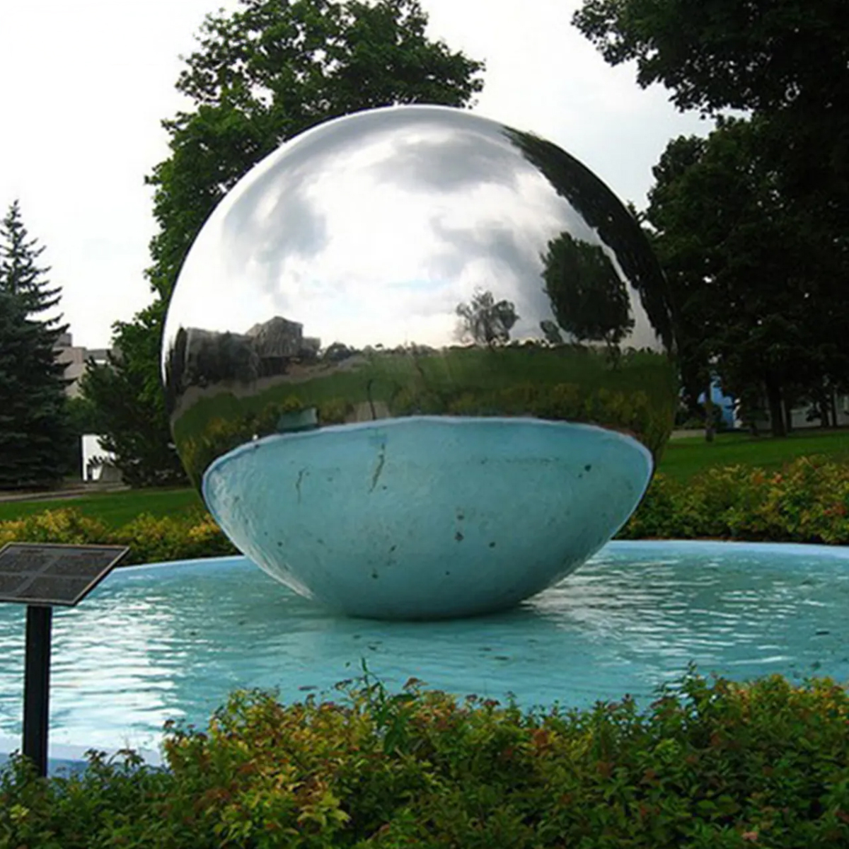 Large stainless steel ball sculpture partially submerged in a water fountain