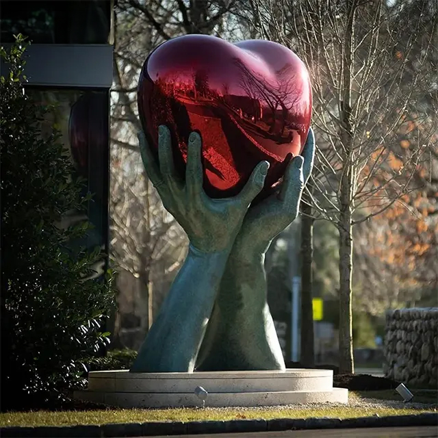 Red Stainless Steel Heart Sculpture held by large bronze hands