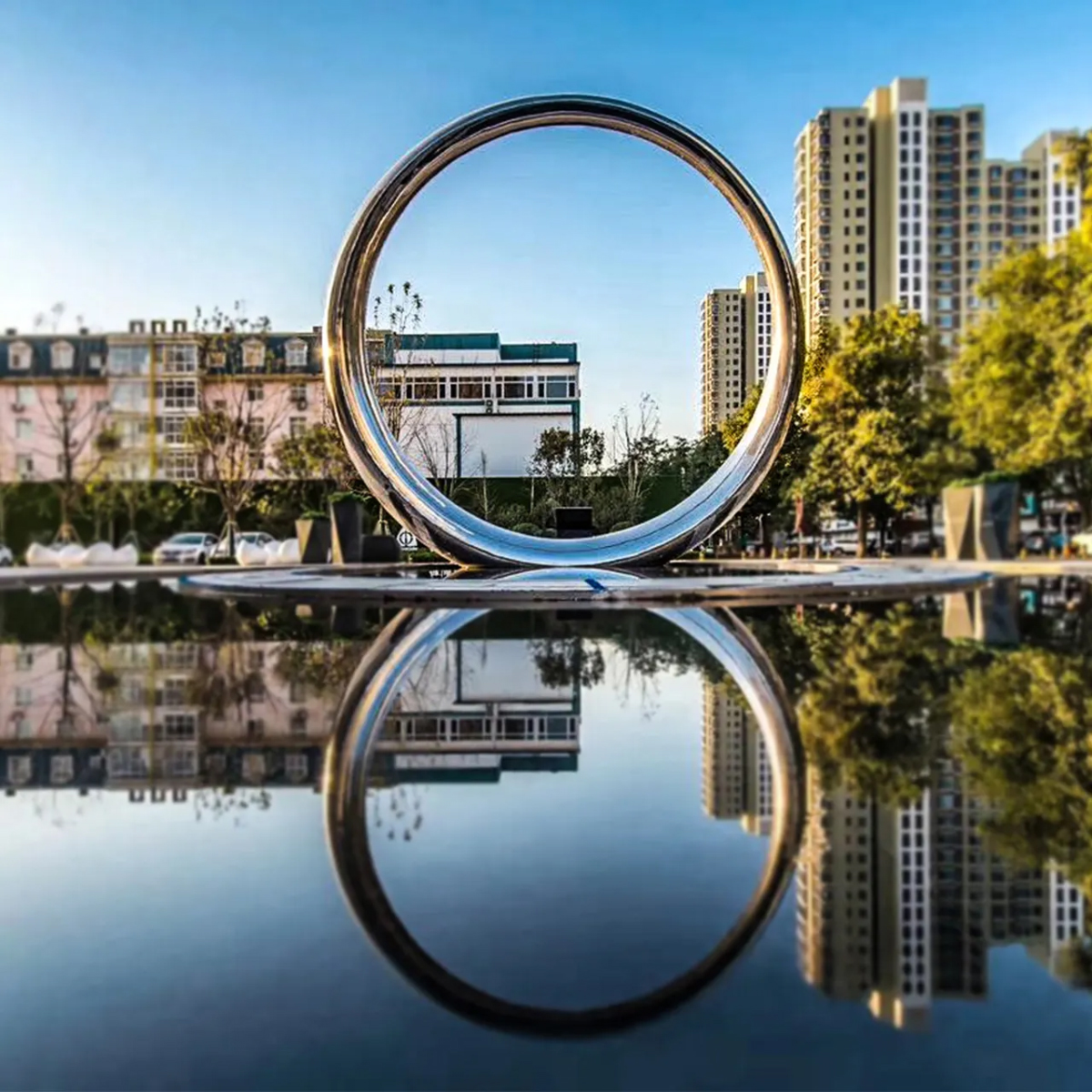 Stainless steel Ring Sculpture placed beside a still pool