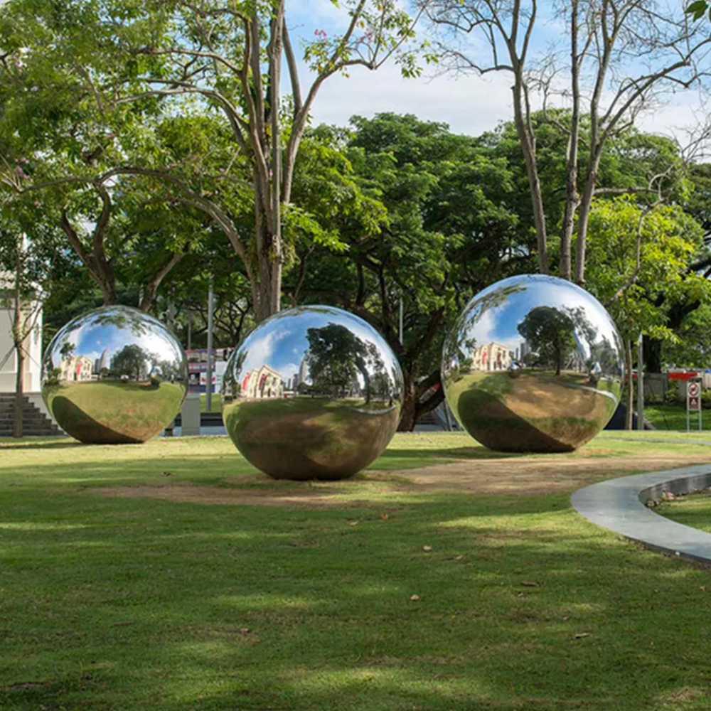 Three mirror polished stainless steel ball sculptures installed in a green urban park