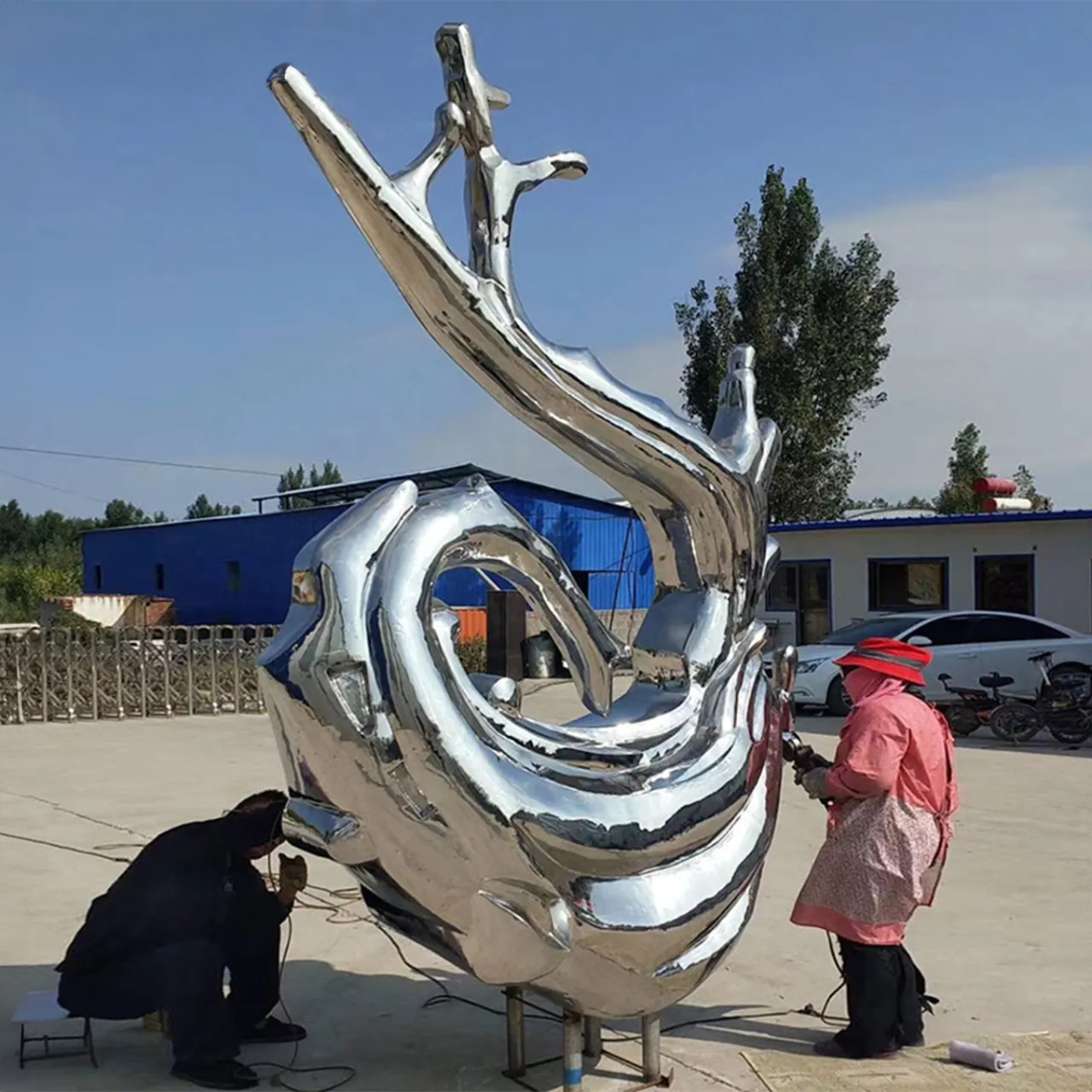 Two workers polishing a large stainless steel Wave Art Sculpture outdoors