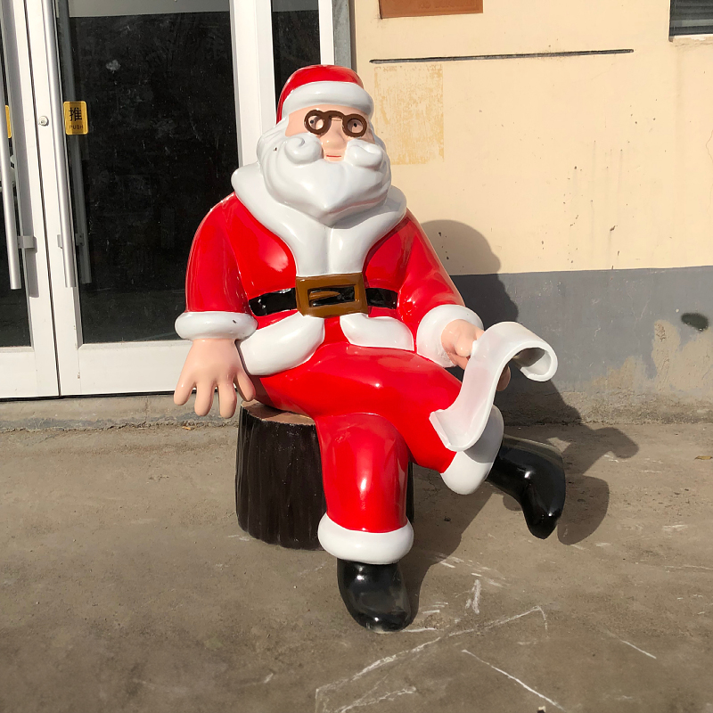 Large Outdoor Santa Statue, fiberglass - made, shows a Santa in classic red suit sitting on a stump