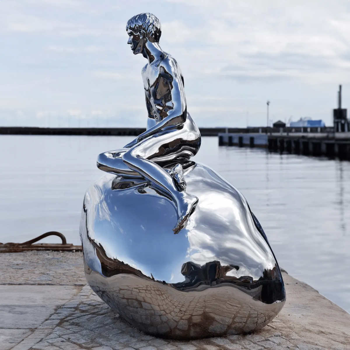 Male Mermaid Statue in polished stainless steel seated on a smooth stone