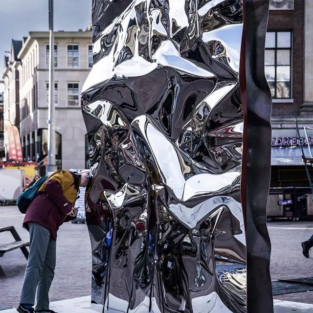 Person interacting with reflective stainless steel Mirror Art Sculpture