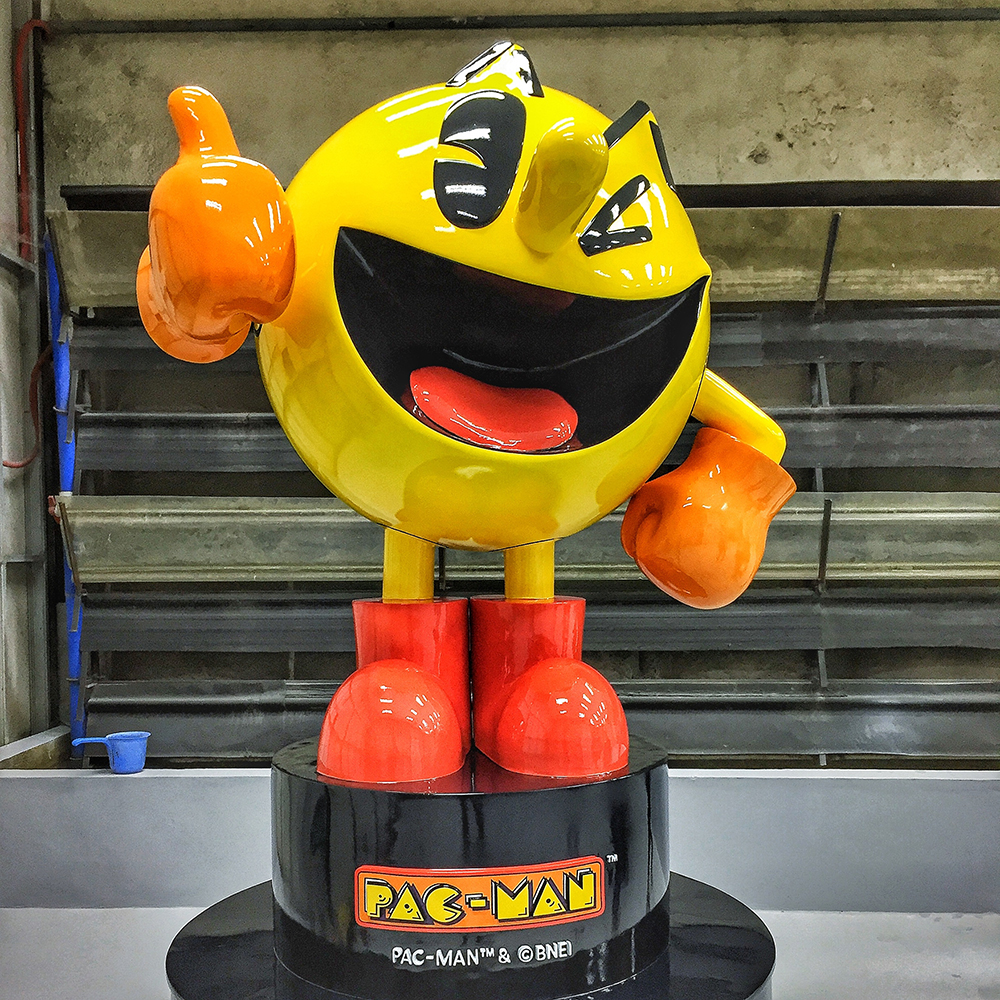 Fiberglass Pac Man Sculpture with bright yellow body, orange gloves, and red boots, smiling