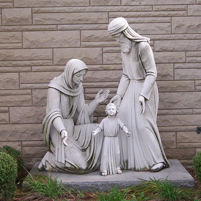 Stone holy family statue outdoor by brick wall