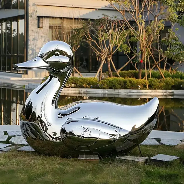 Metal duck statue beside reflective pond